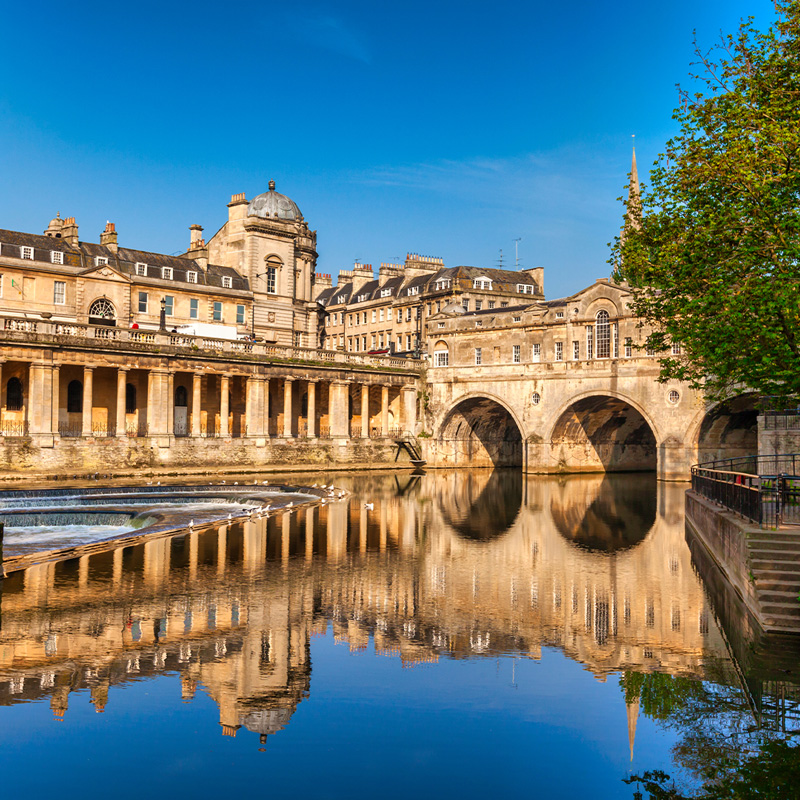 Pulteney Bridge and Weir on the River Avon in the historic city of Bath in Somerset, England, on a bright spring morning with deep blue sky. Stunning reflection, which is genuine.